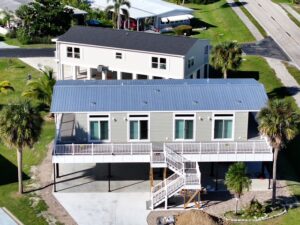 Modern double-wide manufactured home elevated on stilts with front deck and palm trees in a landscaped mobile home community.