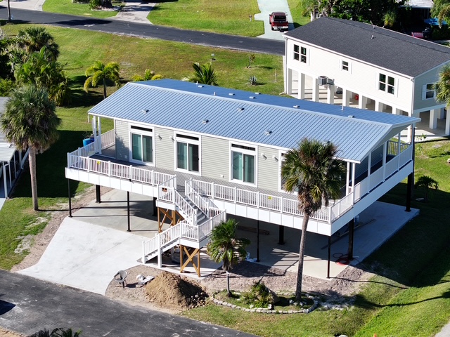 Modern double-wide manufactured home elevated on stilts with front deck and palm trees in a landscaped mobile home community.