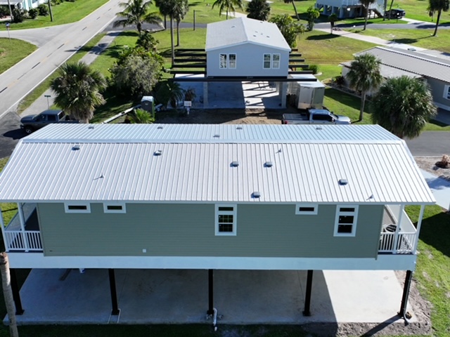 Modern double-wide manufactured home elevated on stilts with front deck and palm trees in a landscaped mobile home community.